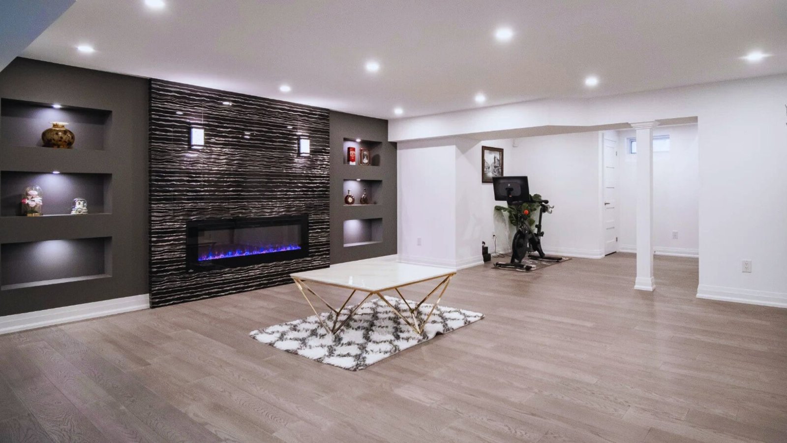 Modern living room with a sleek electric fireplace, built-in shelves, and decorative items. Light wood flooring and a chic glass coffee table add elegance.
