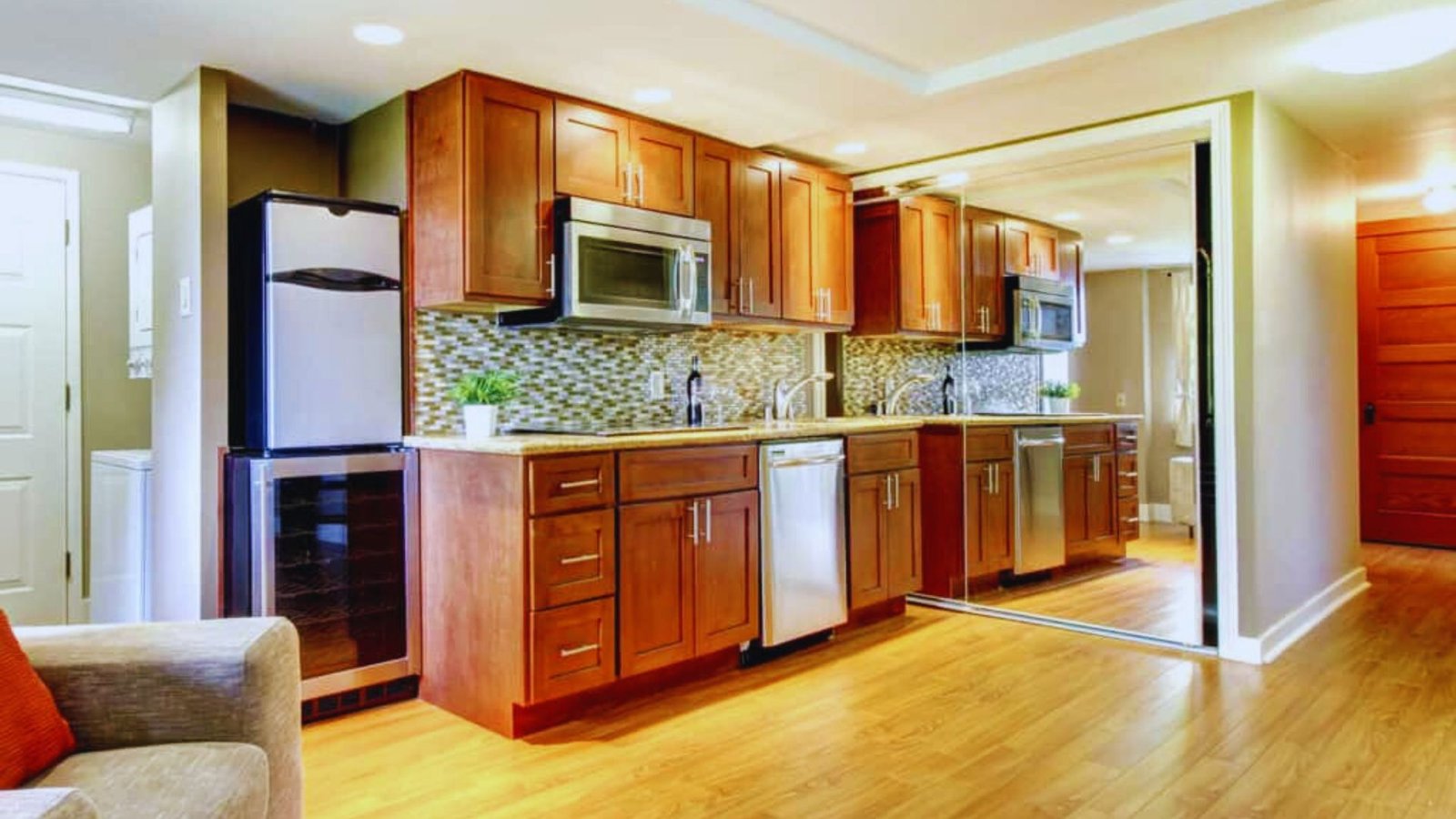 Modern kitchen with warm wooden cabinets, stainless steel appliances, and a patterned tile backsplash. Bright lighting and hardwood floors create an inviting atmosphere.