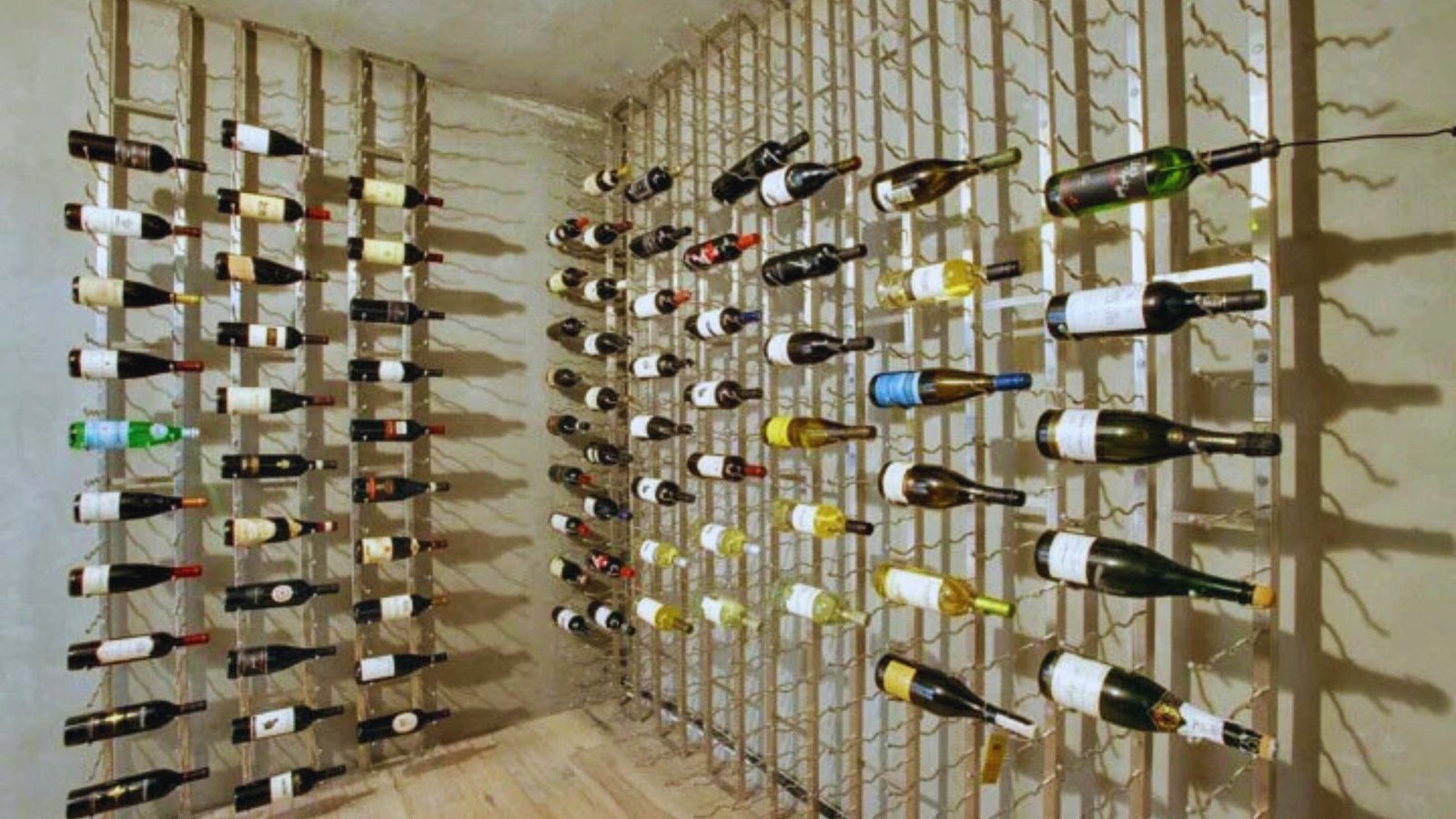 Minimalist wine cellar with bottles displayed horizontally on metal racks against bare walls. The modern design creates a neat, organized look.