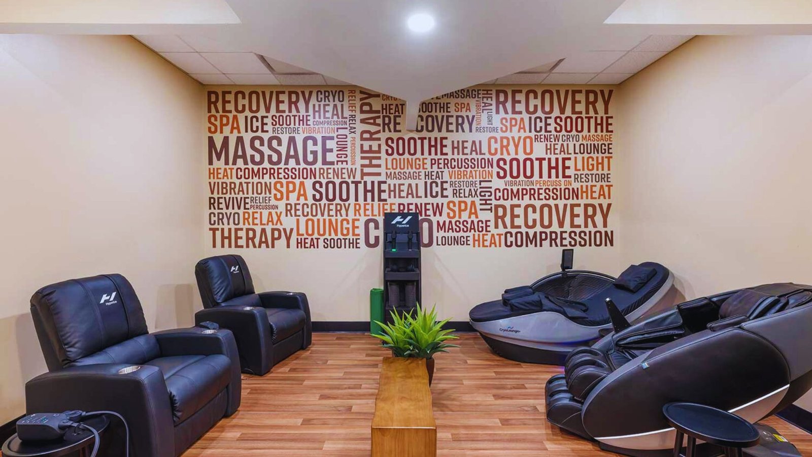 A cozy massage room with leather chairs and recliners on wooden flooring. Walls feature soothing words like 