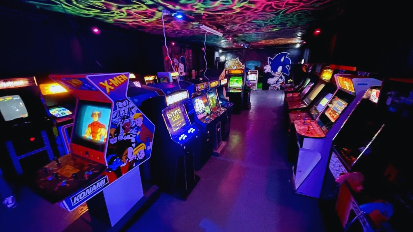 A dimly lit retro arcade with rows of colorful arcade machines lining both sides. A vibrant, glowing ceiling and wall art create a nostalgic vibe. /></p>
<p>Classic arcade machines, neon signs, and vintage-influenced decor bring nostalgic fun to any lower level. It’s a hit with both kids and adults who grew up in the arcade era. Keep the flooring durable and easy to clean for high-traffic play areas.</p>
<h3>14. Billiards Room With Statement Chandelier</h3>
<p><img decoding=