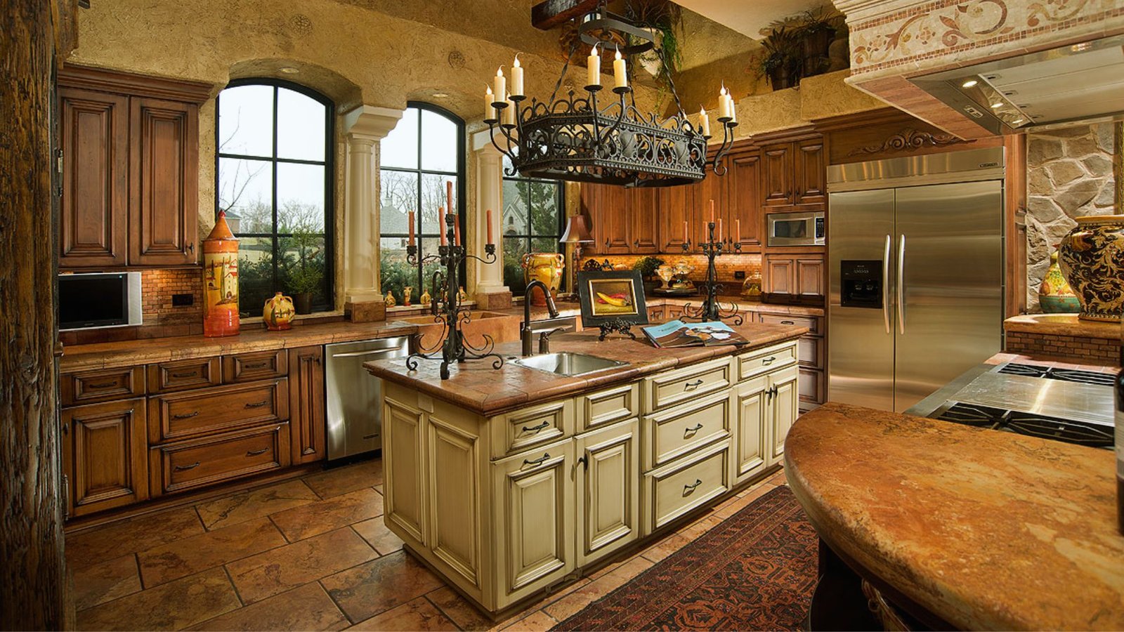 Elegant kitchen with rustic charm; features wooden cabinets, large windows, a central island with chandeliers, stainless steel appliances, and warm lighting.