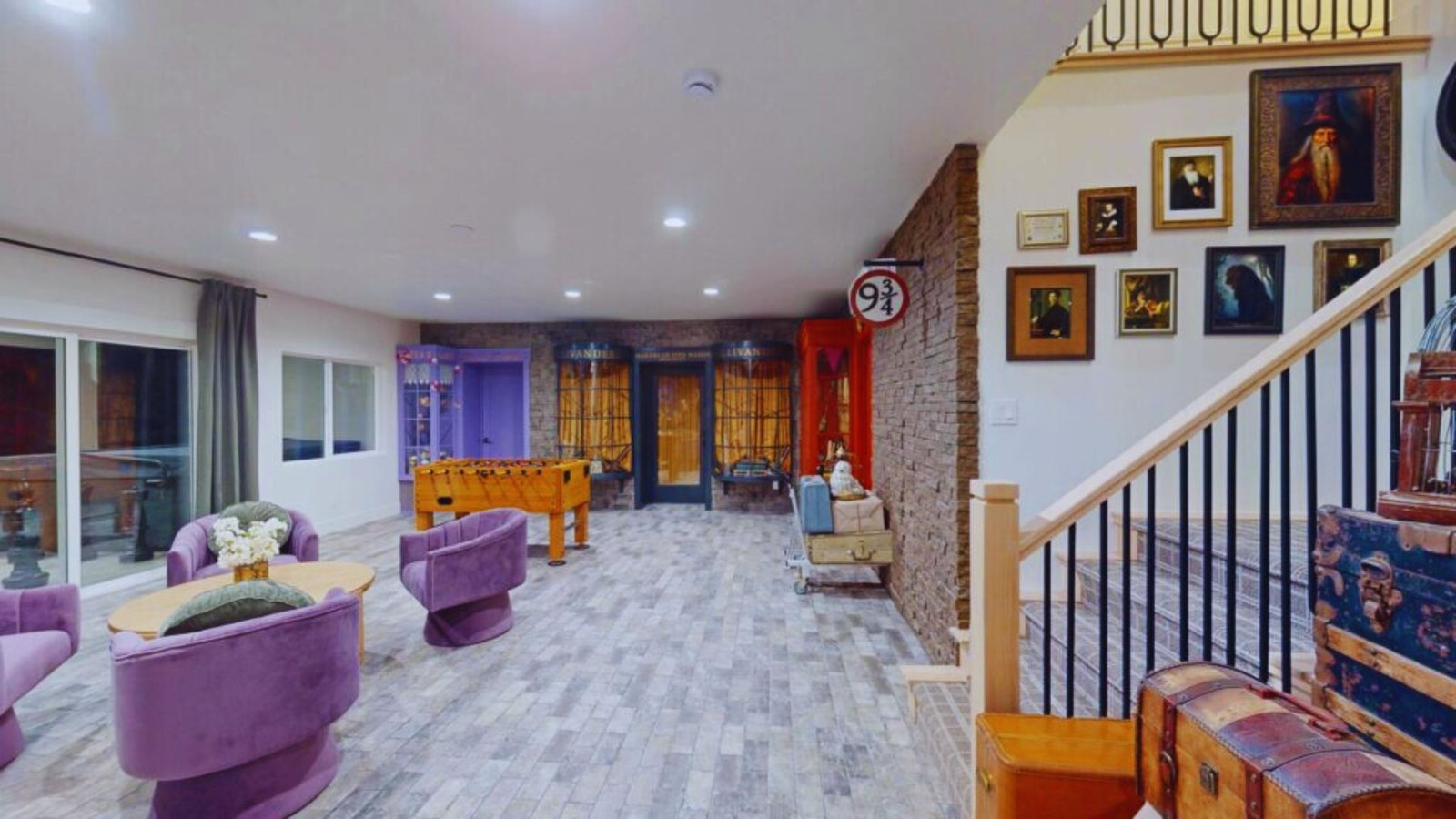 Spacious room with purple chairs around a table, foosball table, brick accent wall, eclectic decor, and framed artwork, creating a cozy, quirky atmosphere.