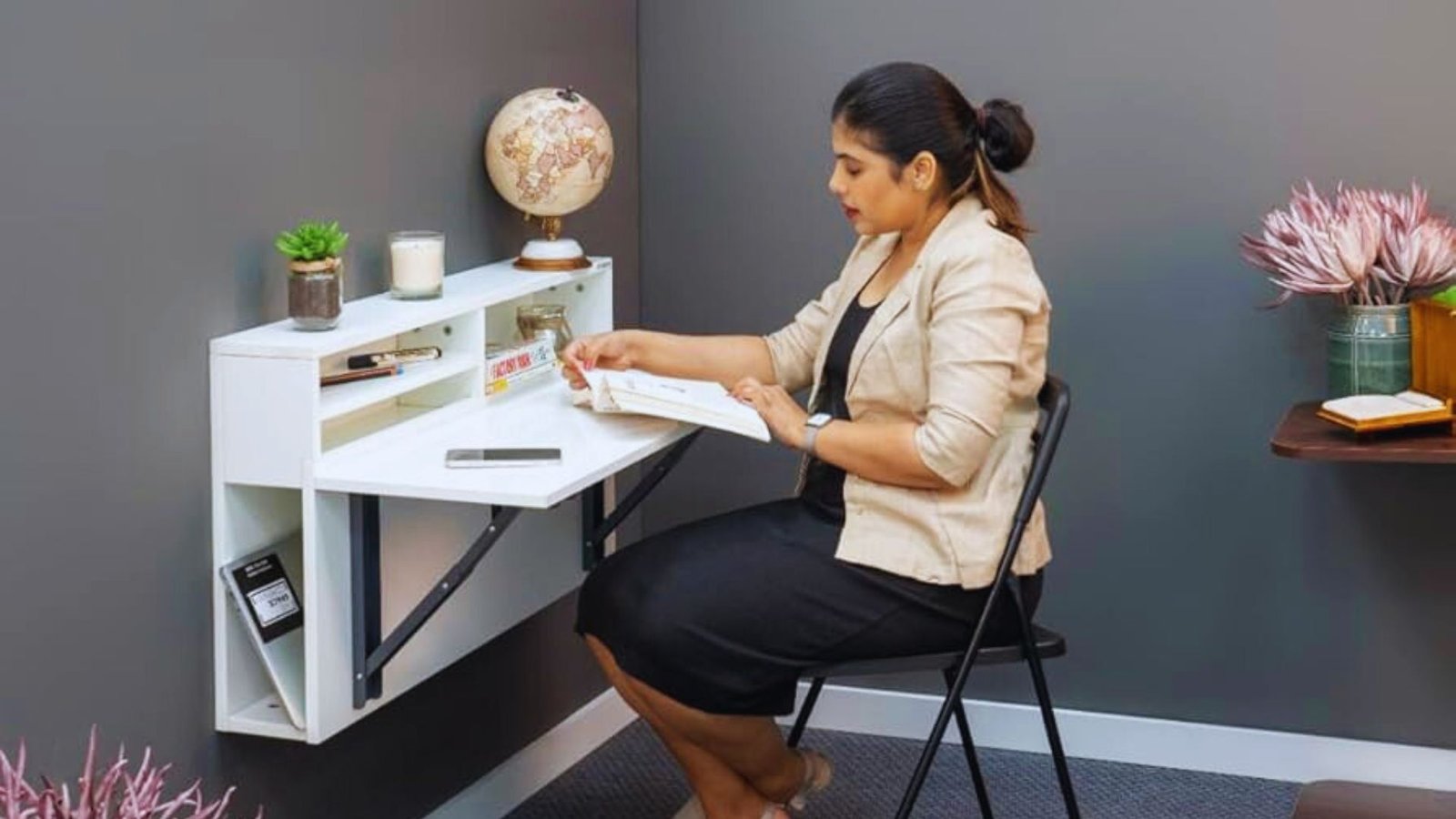 A woman seated at a desk, focused on her laptop, with a notepad and pen beside her.