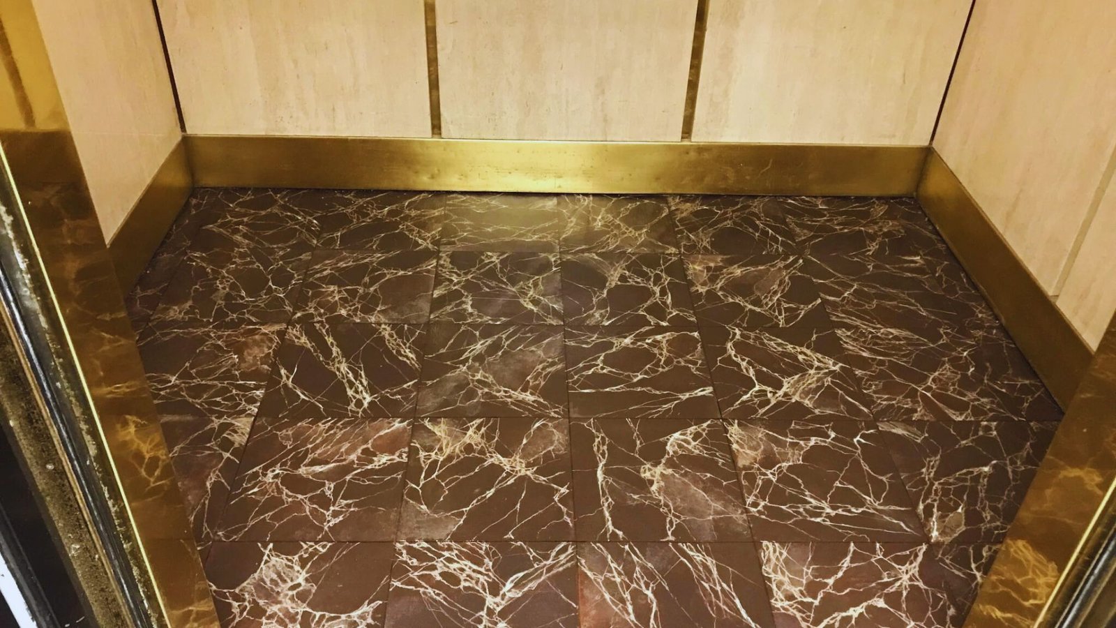  An elevator interior showcasing a polished marble floor with luxurious gold trim.