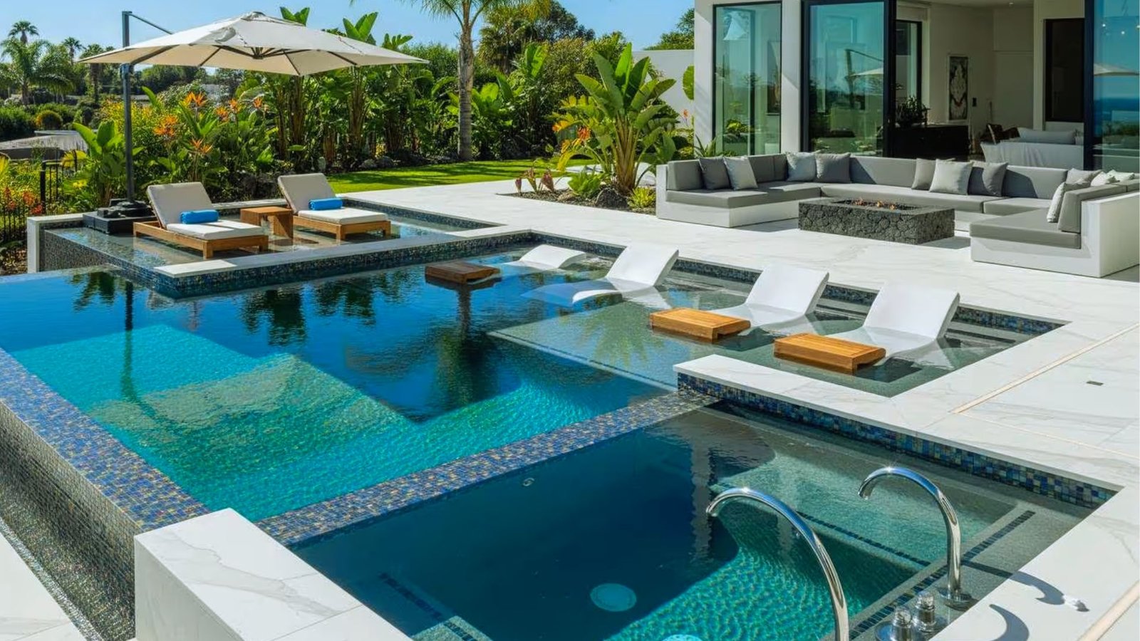pool with loungers and umbrellas is situated in front of a house, creating a relaxing outdoor space.