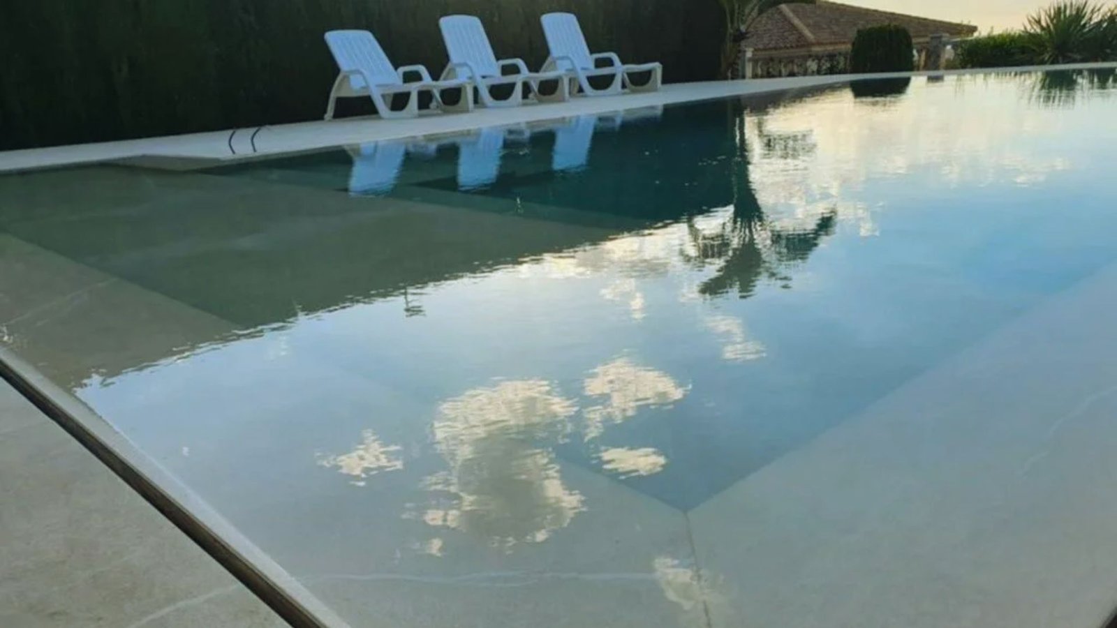 A calm swimming pool with chairs nearby, showcasing a reflection of the sky.