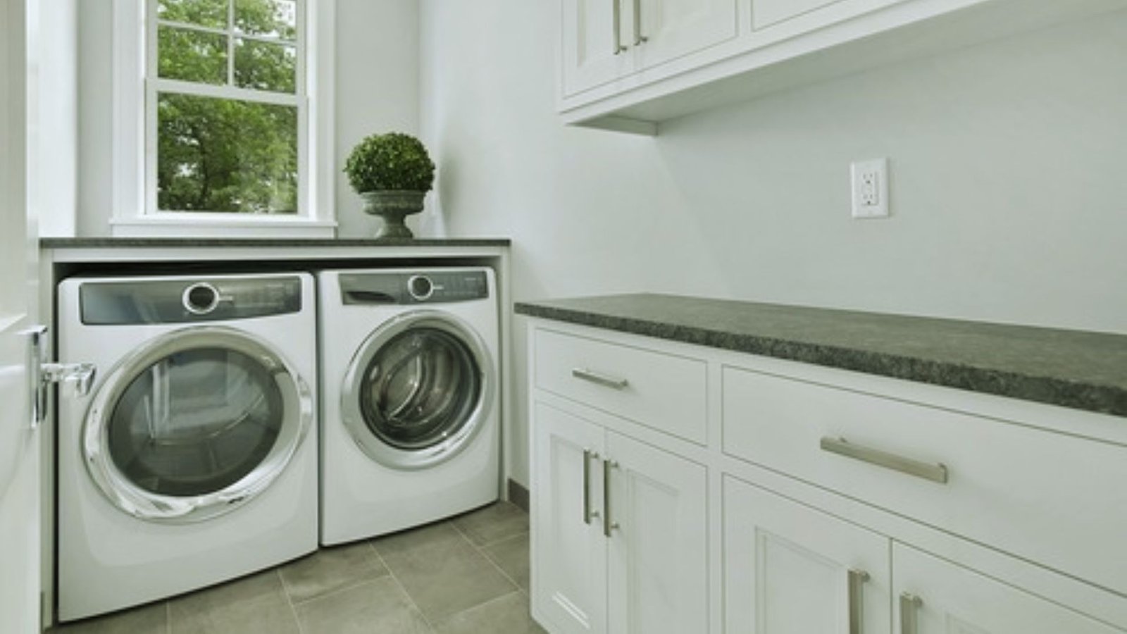 A laundry room featuring a washer and dryer, with shelves and laundry supplies visible in the background.