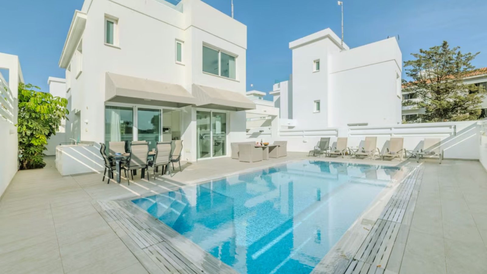 A sleek modern villa featuring a spacious swimming pool surrounded by lush greenery.