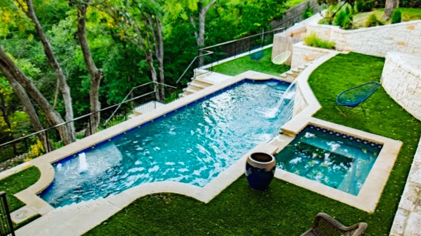 A backyard pool surrounded by a grassy area and a stone wall, creating a serene outdoor space for relaxation.