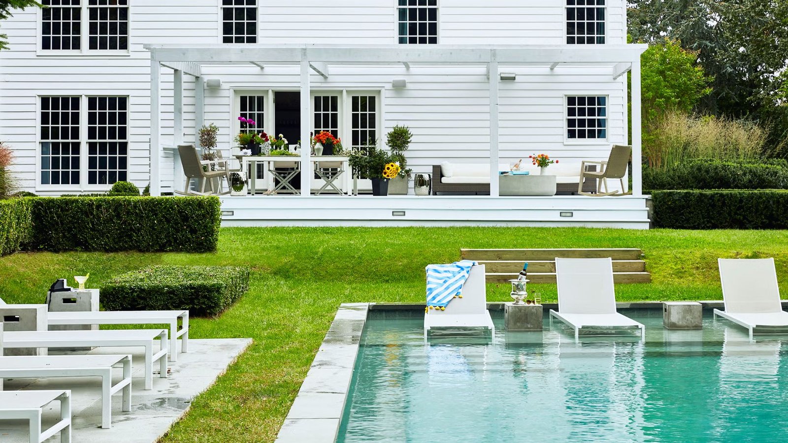 A white house with a swimming pool and several lawn chairs set up for relaxation.