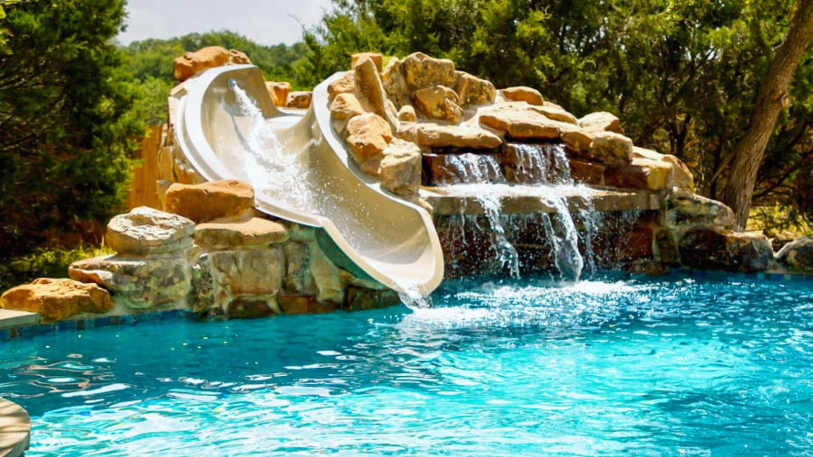 A swimming pool featuring a slide and a cascading waterfall, surrounded by lush greenery.