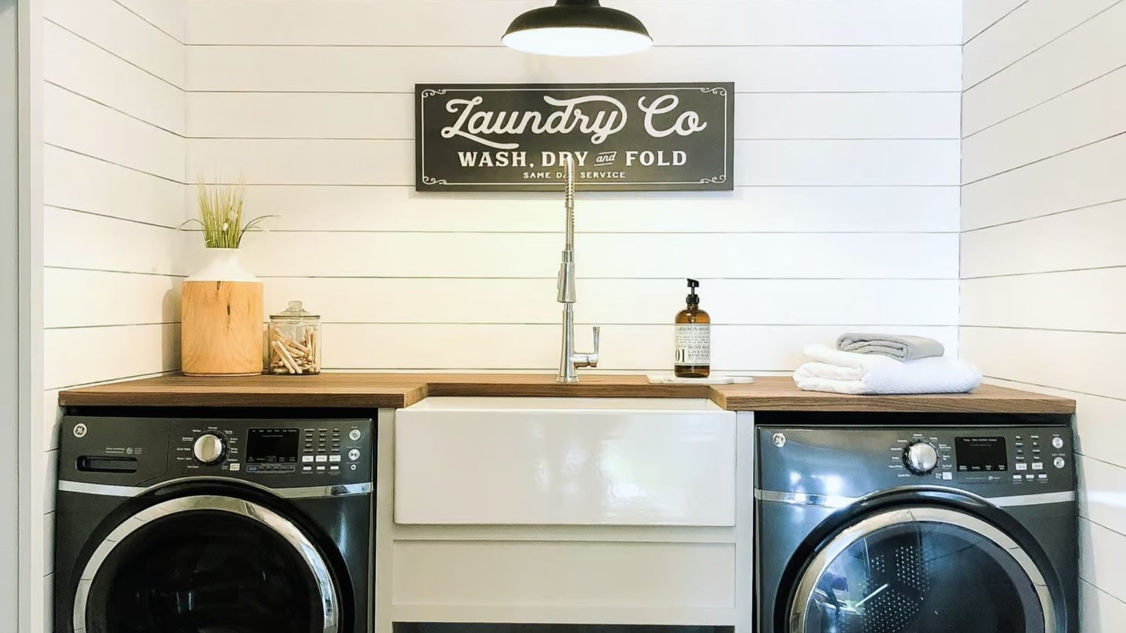 A laundry room featuring a washer and dryer, with shelves and laundry supplies visible in the background.
