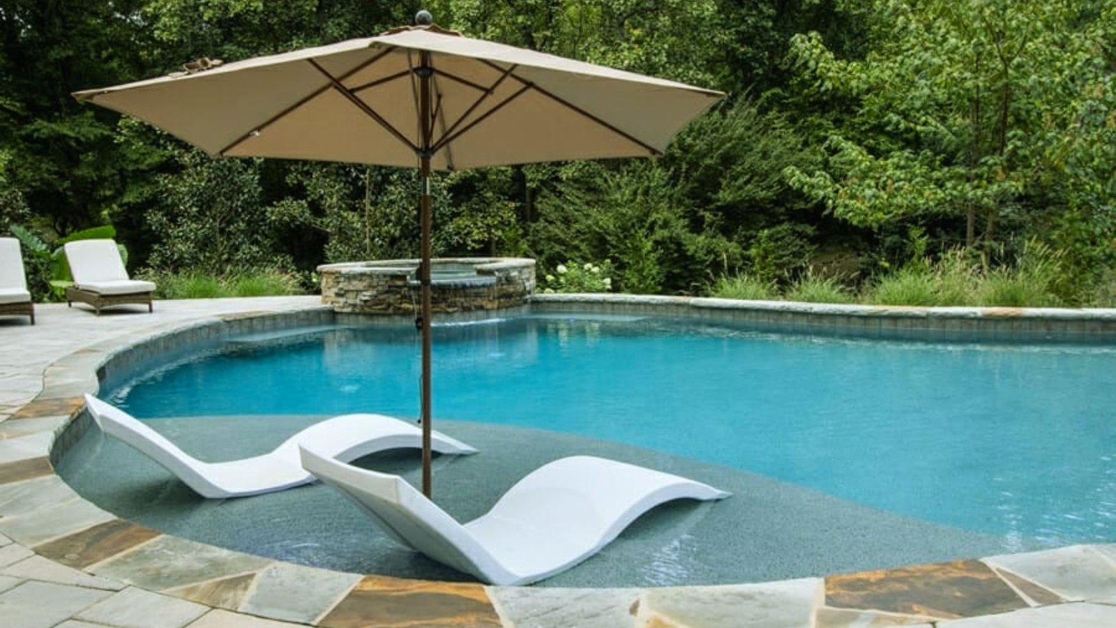 A serene pool scene featuring two lounge chairs and a large umbrella for shade.