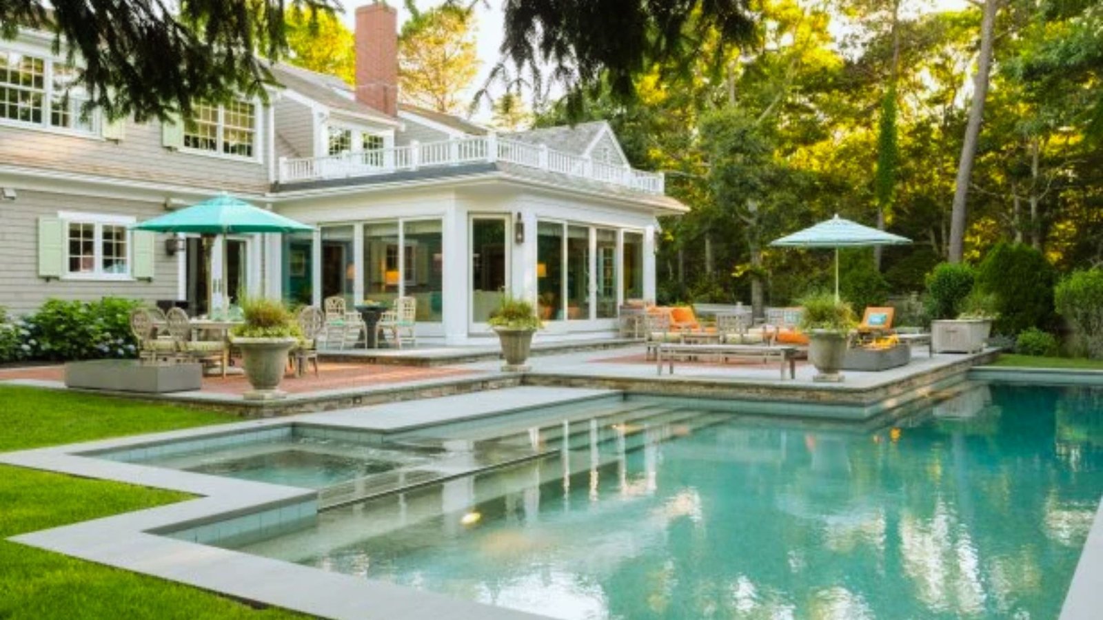 A pool and patio area situated in front of a house, featuring lounge chairs and a clear blue water surface.