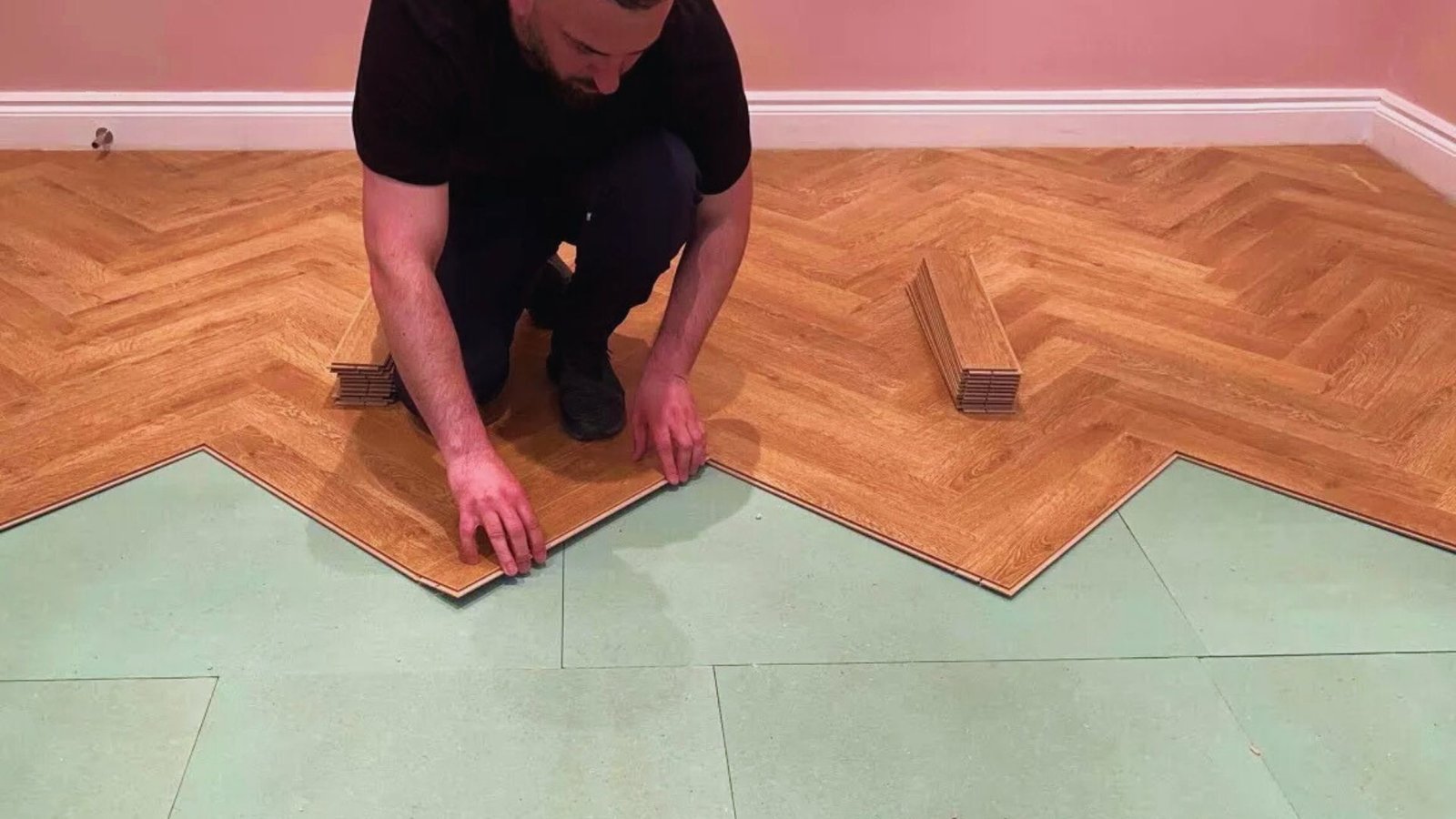 A man is installing wooden floorboards, carefully laying them down on a subfloor.