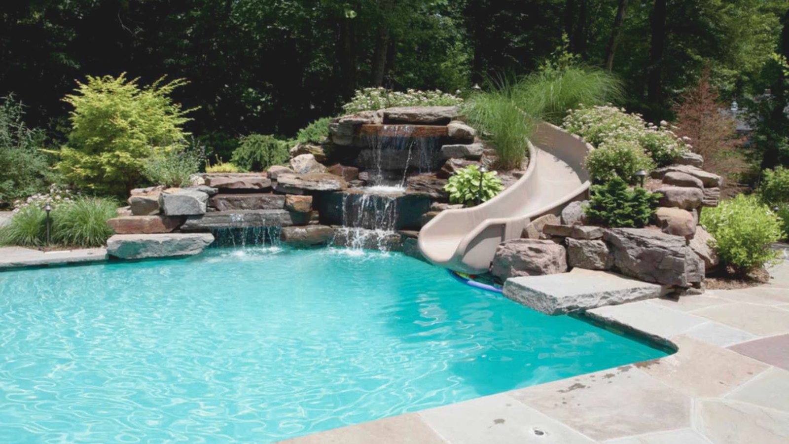 A vibrant pool with a fun slide and an elegant water feature, inviting for relaxation and play.