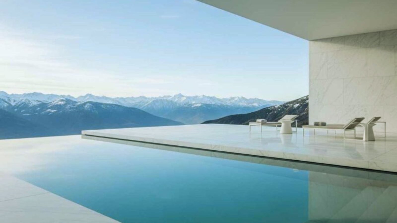 A tranquil pool area with chairs offers a breathtaking view of a majestic mountain range in the distance.
