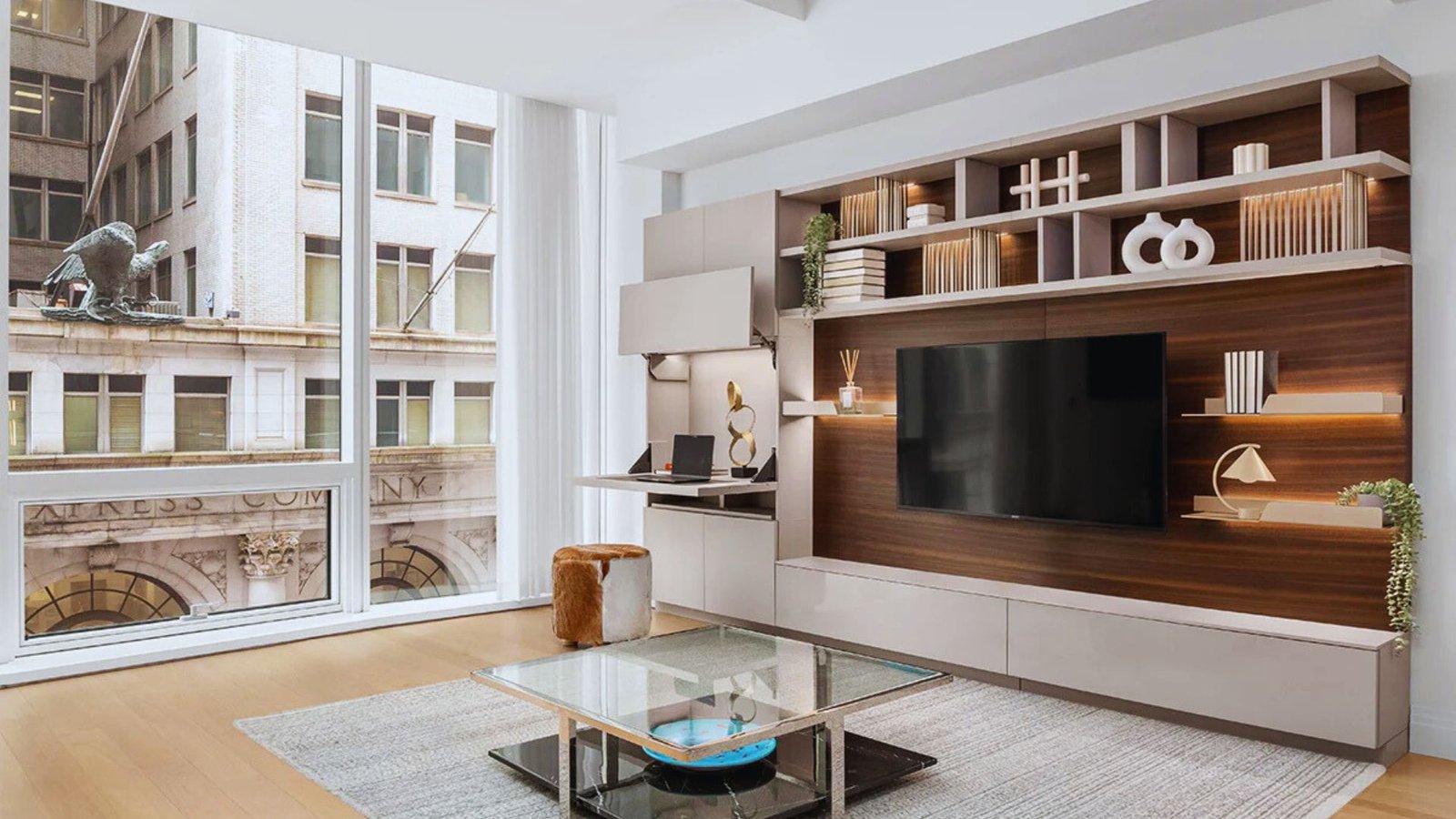 A cozy living room featuring a TV, a bookshelf filled with books, and a large window letting in natural light.