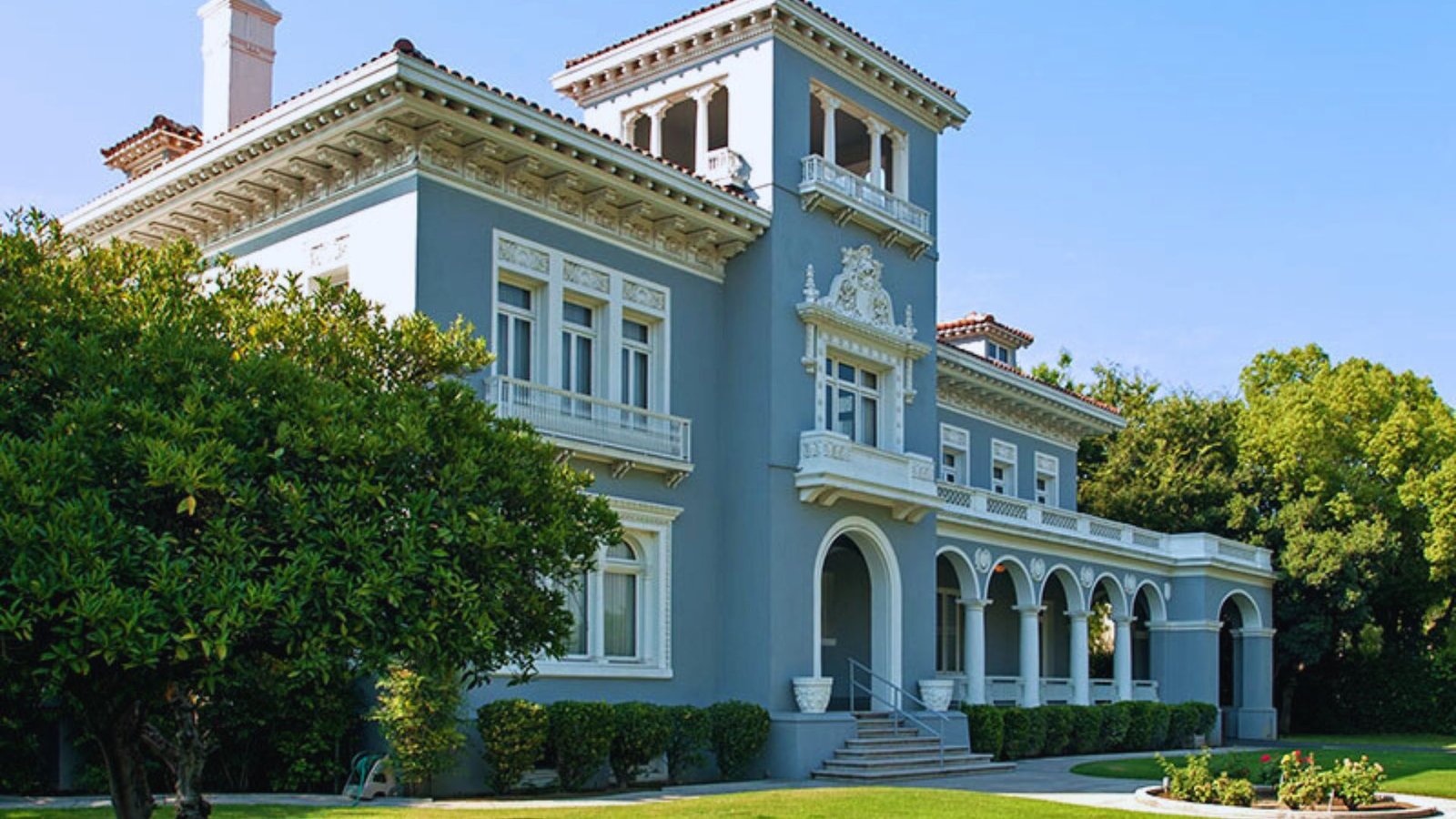 A large blue mansion with white trim stands prominently on a well-maintained lawn.