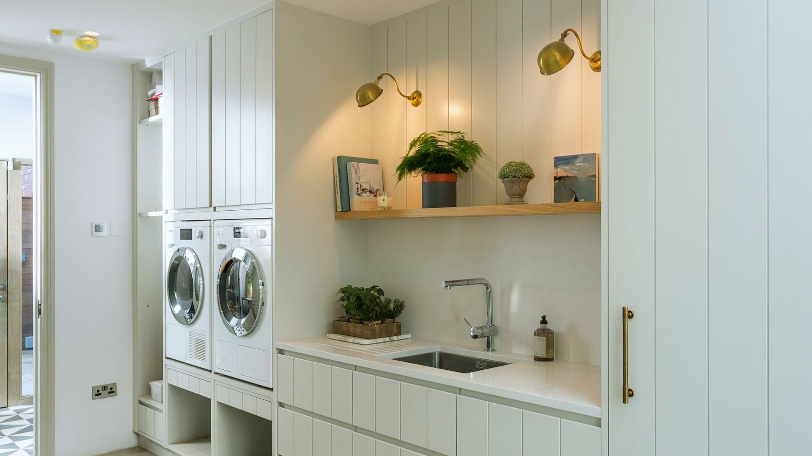 A modern laundry room featuring a sleek sink and a front-loading washer against a bright, organized backdrop.